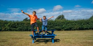 Two boys jumping off a picnic table.