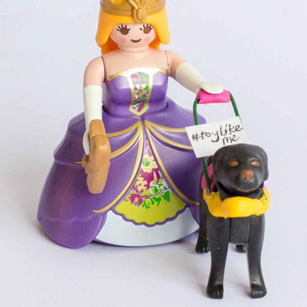 #ToyLikeMe makeover image showing Playmobil princess figure with a guide dog. The guide dog has a pink harness.