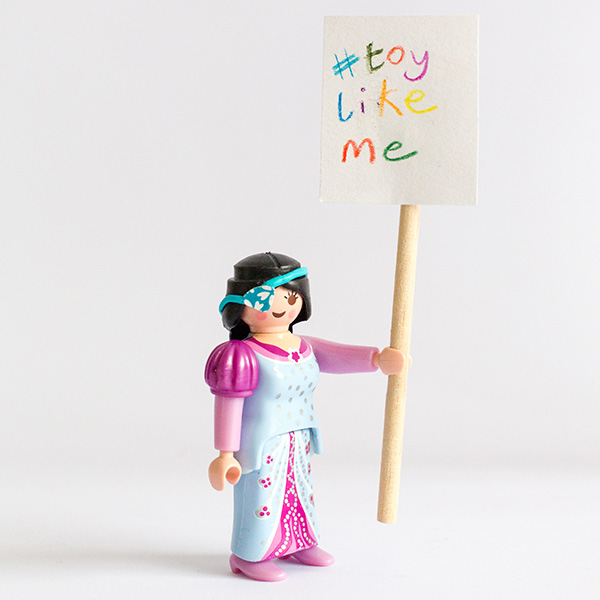 #ToyLikeMe makeover image showing a Playmobil princess figure with a model eye patch. She is holding a sign which reads '#toylikeme'.