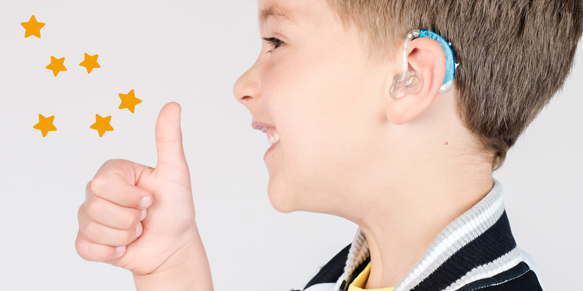 Image shows boy with blue hearing aid giving the thumbs up. There are yellow stars around his thumbs.