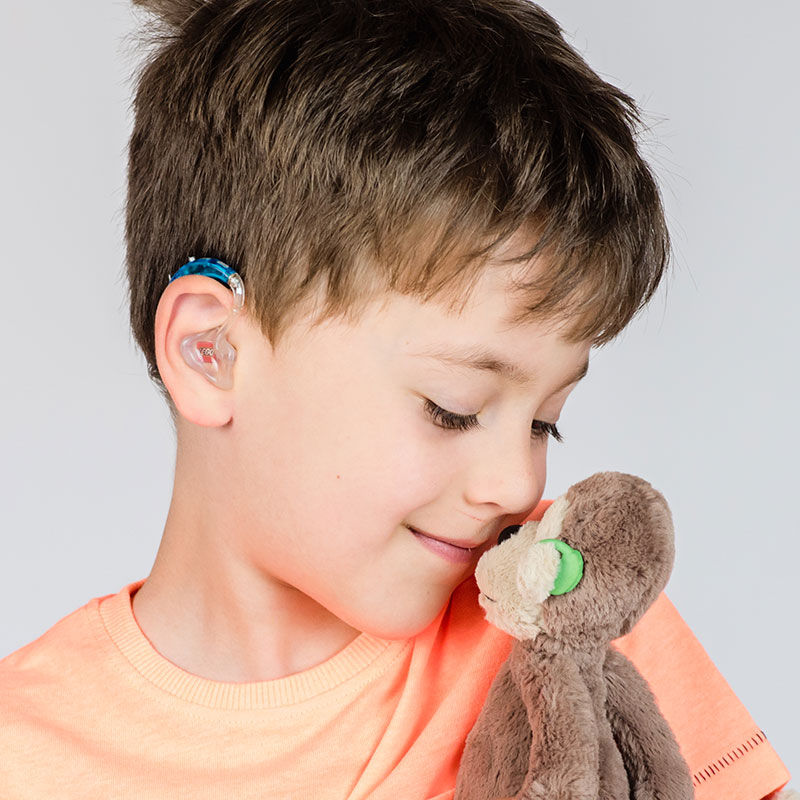 Boy with hearing aid holding a plush monkey, also with a hearing aid.