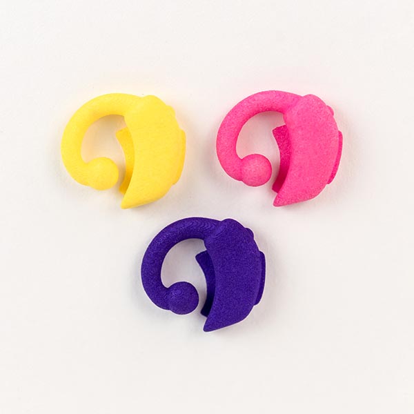 Image shows three 3D prinited hearing aids, in pink, yellow and purple.