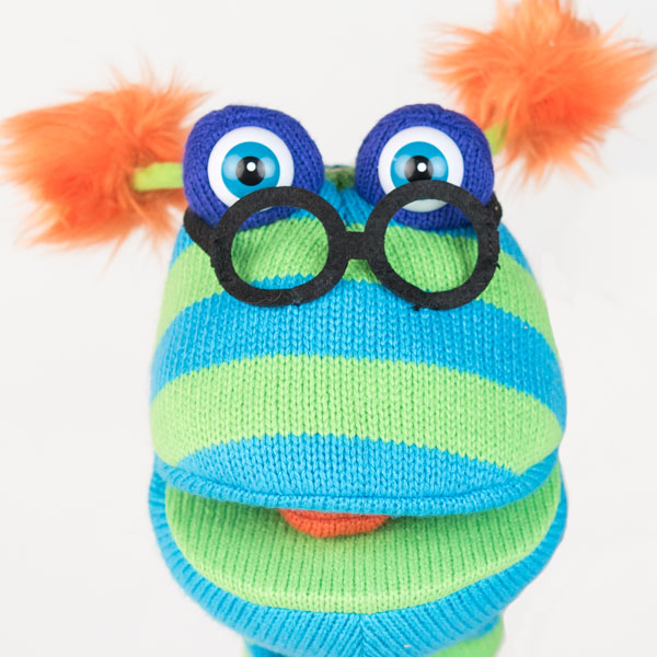 Close up of blue and green striped woolen hand puppet with black glasses and orange fluffy ears.
