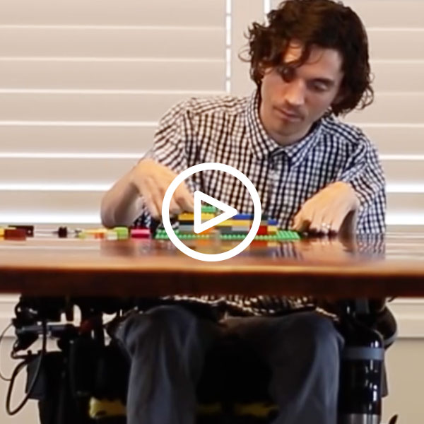 Image shows Dan Harvey at a table playing with Lego. There is a triangle video emblem overlaid.