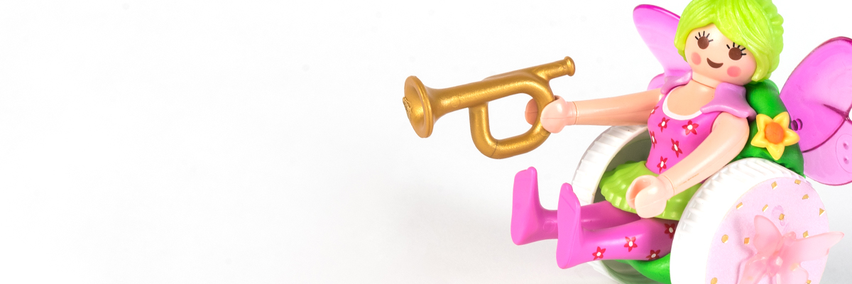 #ToyLikeMe makeover image of Playmobil fairy figure using a pink and green wheelchair made of modelling clay. The back of the chair has pink wings.