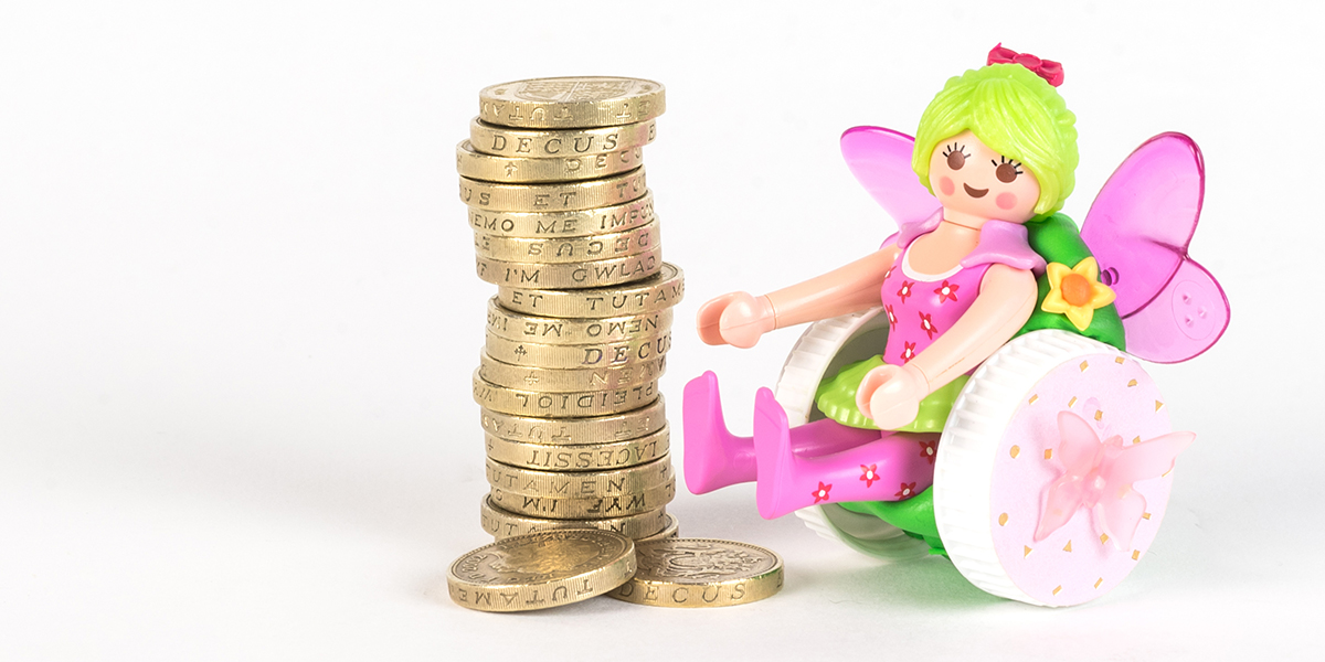 #ToyLikeMe makeover image of Playmobil fairy figure using a pink and green wheelchair made of modelling clay. The back of the chair has pink wings. She is sat next to a pile of one pound coins.