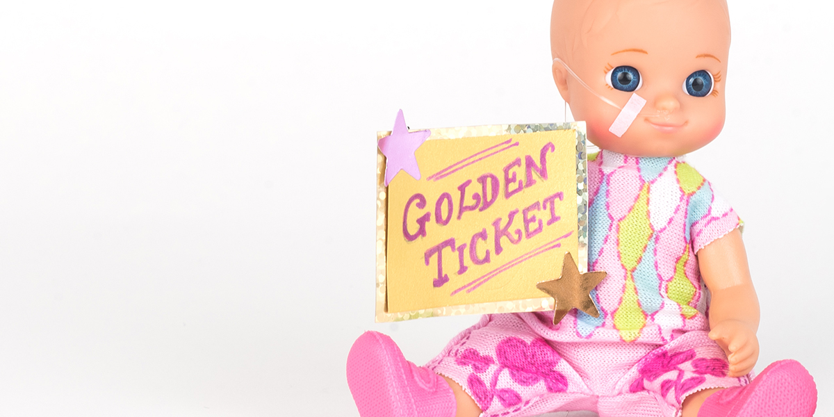 #ToyLikeMe makeover image showing baby girl toy with nasal feeding tube. The doll holding a golden ticket.