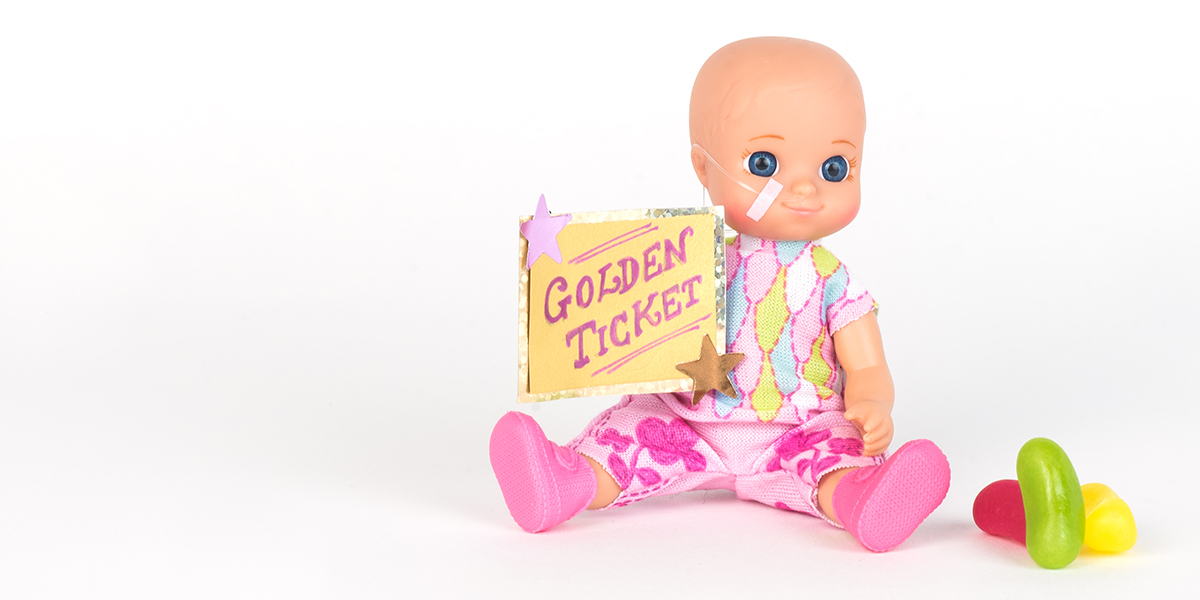 #ToyLikeMe makeover image showing baby girl toy with nasal feeding tube. The doll holding a golden ticket.