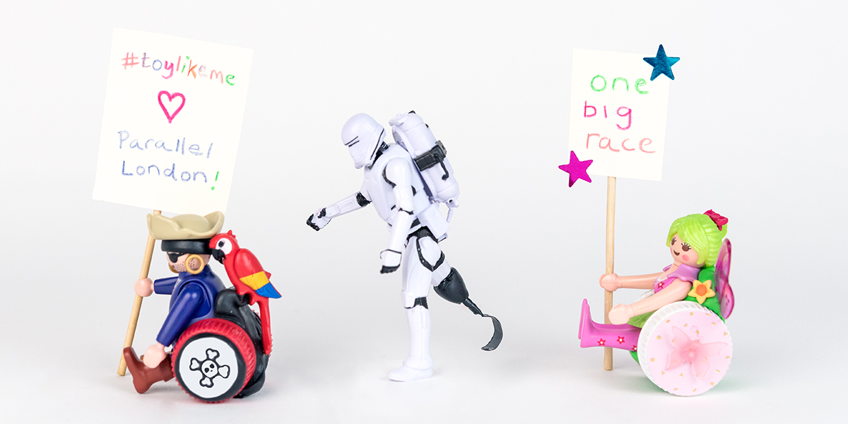 #ToyLikeMe makeover image showing a group of toys with various diff:abilities and carrying a sign which reads '#ToyLikeMe loves Parallel London, one big race,'