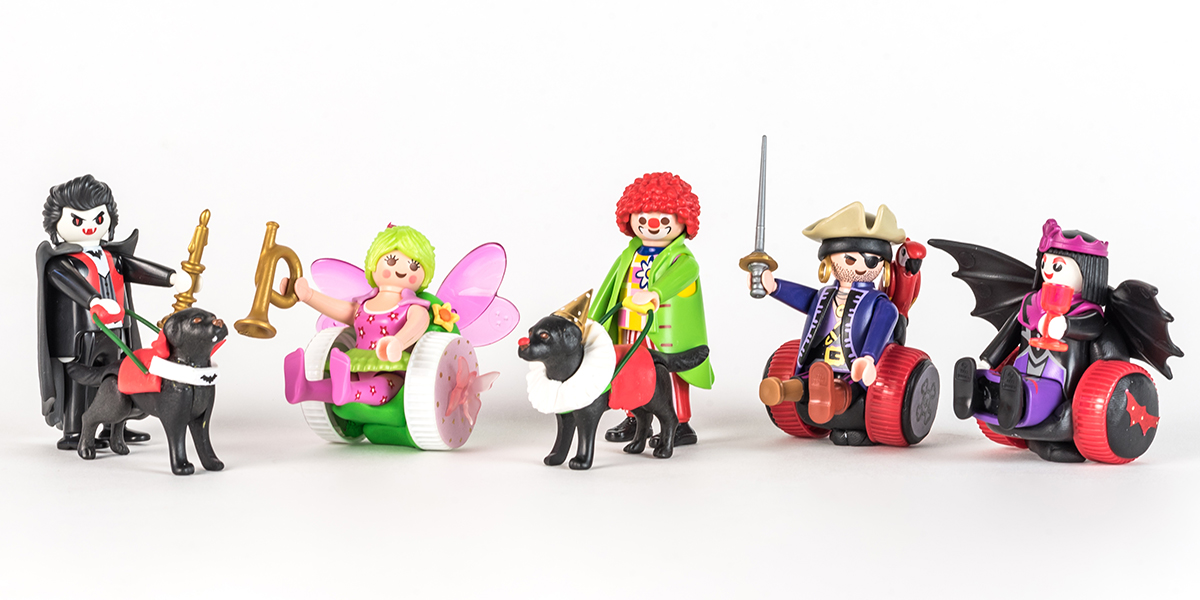#ToyLikeMe makeover image showing a group of Playmobil figures. Dracula and a clown with guide dogs and a fairy, pirate and Draculette with wheelchairs made of modelling clay.