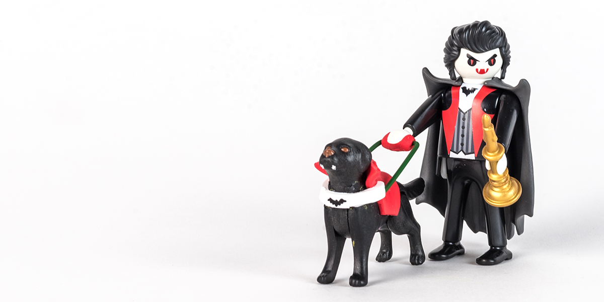 #ToyLikeMe makeover image of Playmobil Dracula figure with a guide dog. The guide dog has fangs and a red harness with a bat on it made of modelling clay.