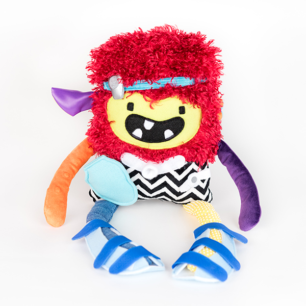 Plush monster from Weesie Pals. Made from a variety of colours and textures of fabric. The monster is also rocking a baha, trach tube, ostomy pouch, g-tube and leg splints.