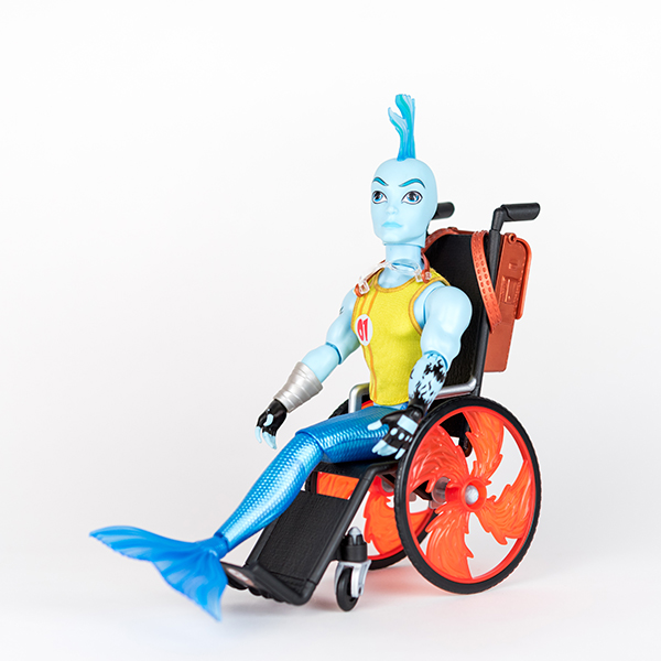 Image shows blue merman figure using a toy wheelchair with orange flaming wheels.