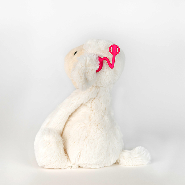 White plush monkey with hot pink 3D printed hearing aid.