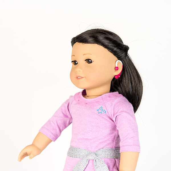 American Girl doll with brown hair, a pale pink dress and hot pink hearing aids.