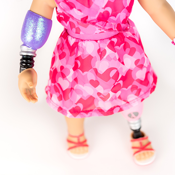 American Girl doll in pink and red dress with prosthetic leg and arm.