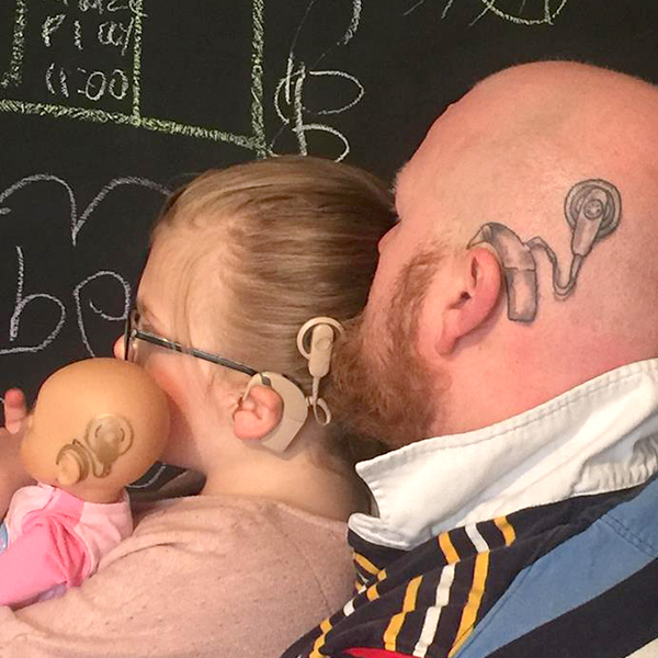 Community makeover image showing a girl, a doll and her dad. All three have cochlear implants. The father's is a tattoo.
