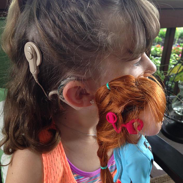 Community makeover image showing girl and Makie doll. Both have matching cochlear implants.
