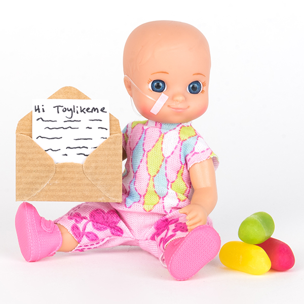 #ToyLikeMe makeover image showing baby girl toy with nasal feeding tube. The doll holding a little envelope.