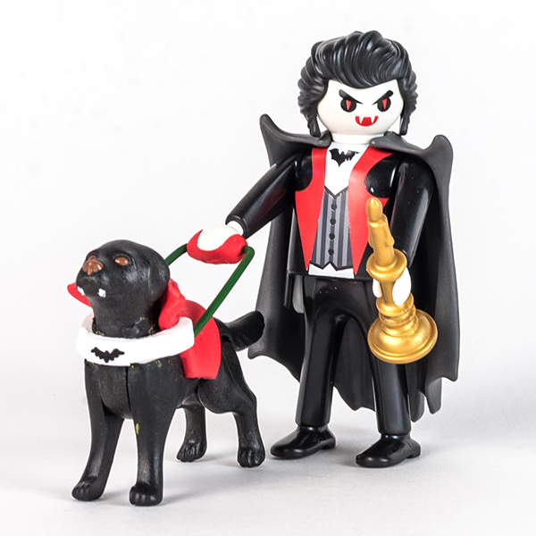 #ToyLikeMe makeover image of Playmobil Dracula figure with a guide dog. The guide dog has fangs and a red harness with a bat on it made of modelling clay.
